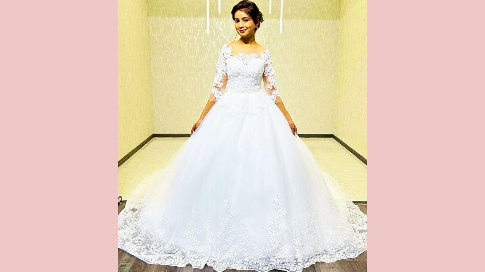 Smiling bride in classic ballgown with lace illusion neckline, three-quarter sleeves, full tulle skirt, lace hem, standing indoors