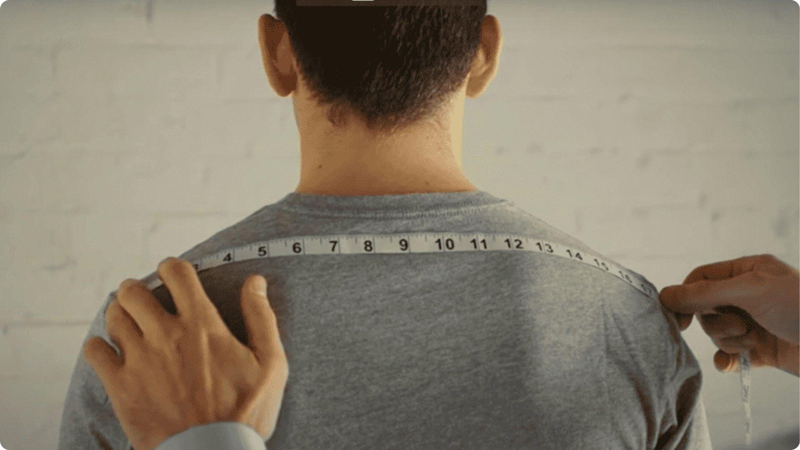 Measuring tape stretched across the back of a man from shoulder point to shoulder point.