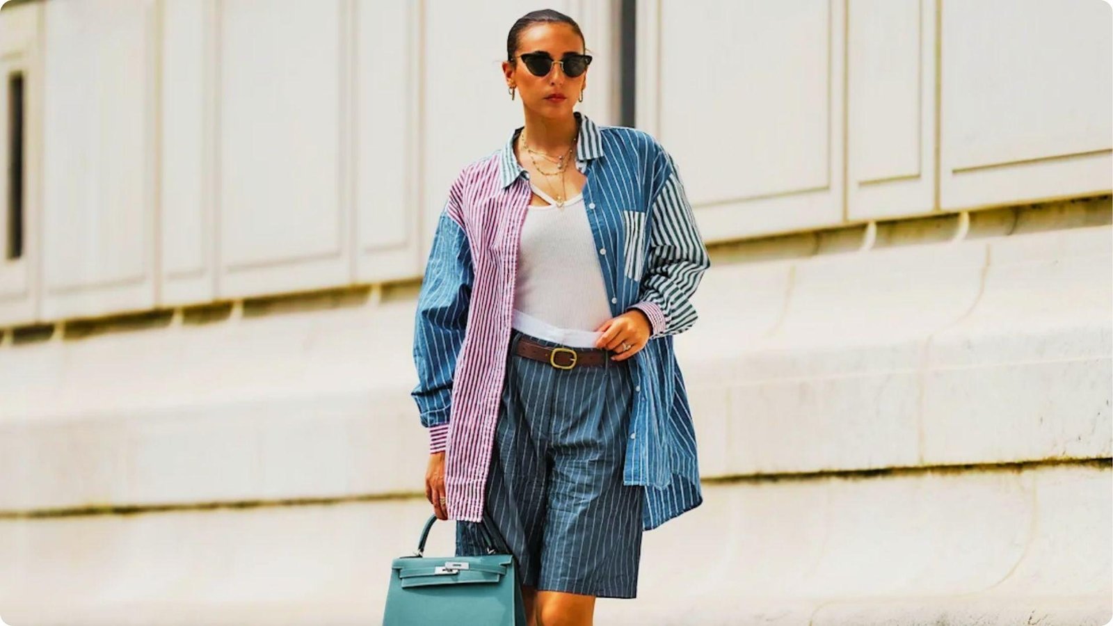 Woman in a color-blocked oversized striped shirt worn open over a white ribbed tank top and pinstripe shorts.