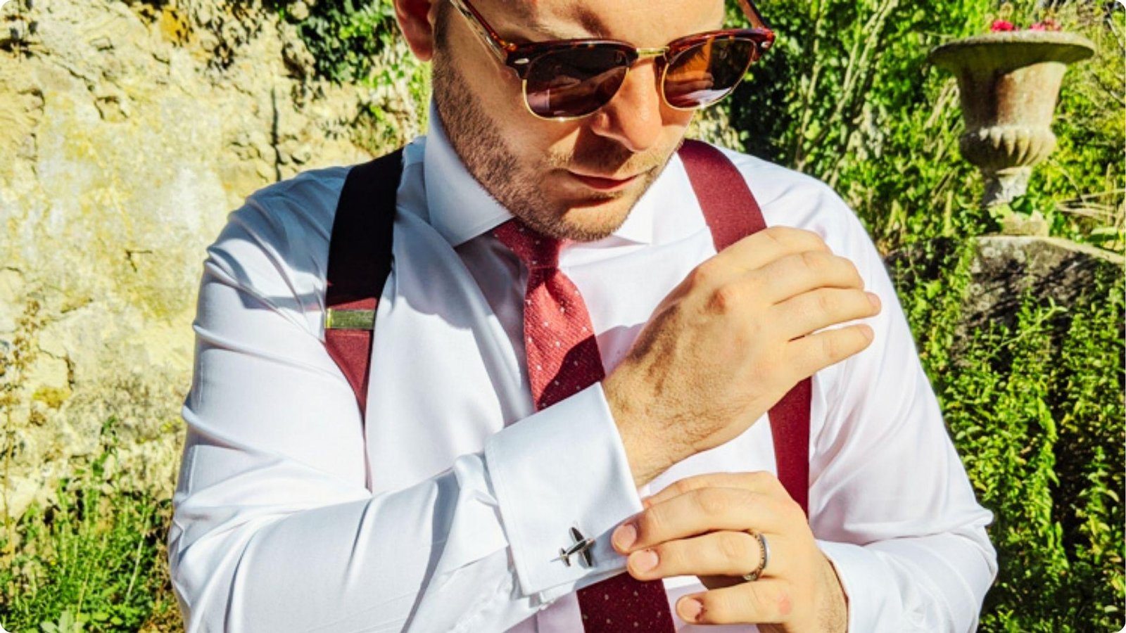 Man in sunglasses and suspenders adjusting his dress shirt cuff with an airplane cufflink.