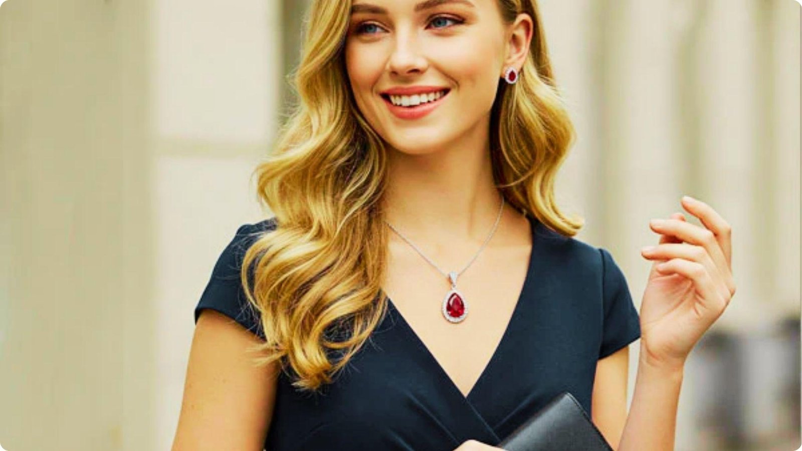 Smiling woman in a navy wrap dress styled with ruby teardrop pendant necklace, matching earrings, and a black clutch.