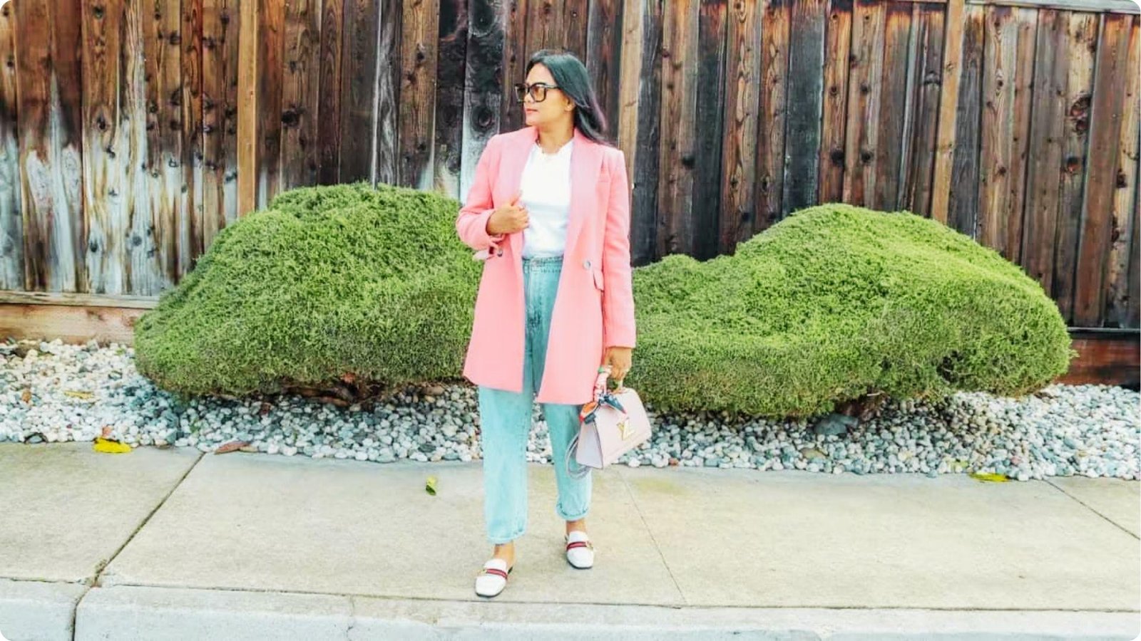 Woman stands outdoors in a pastel pink coat layered over light-wash blue jeans.
