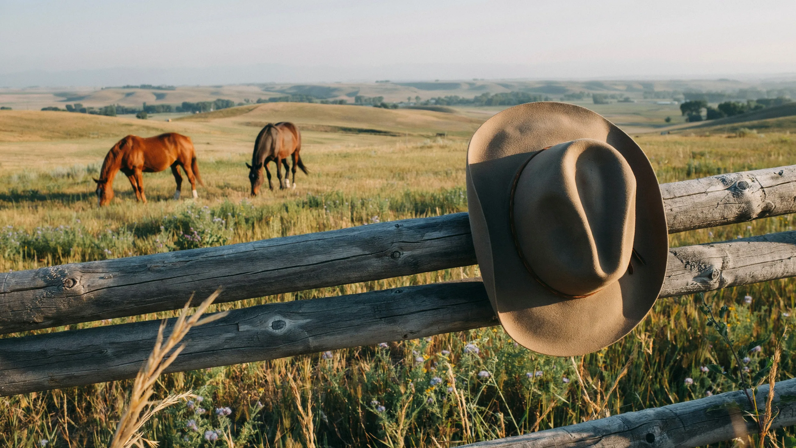 Classic cowboy hat displayed on a ranch fence at sunset.