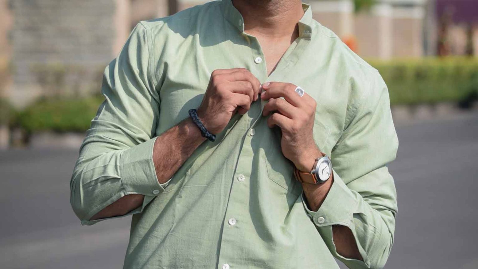 A man in a green shirt is seen adjusting his shirt, embodying an effortless and fashionable look.