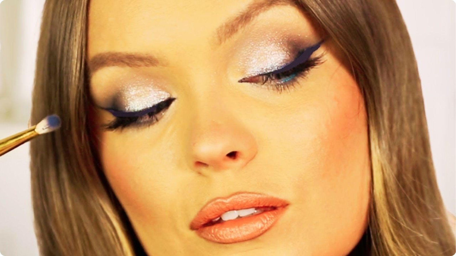 Close-up of a woman’s eye with shimmery silver eyeshadow and bold navy blue winged eyeliner being applied.