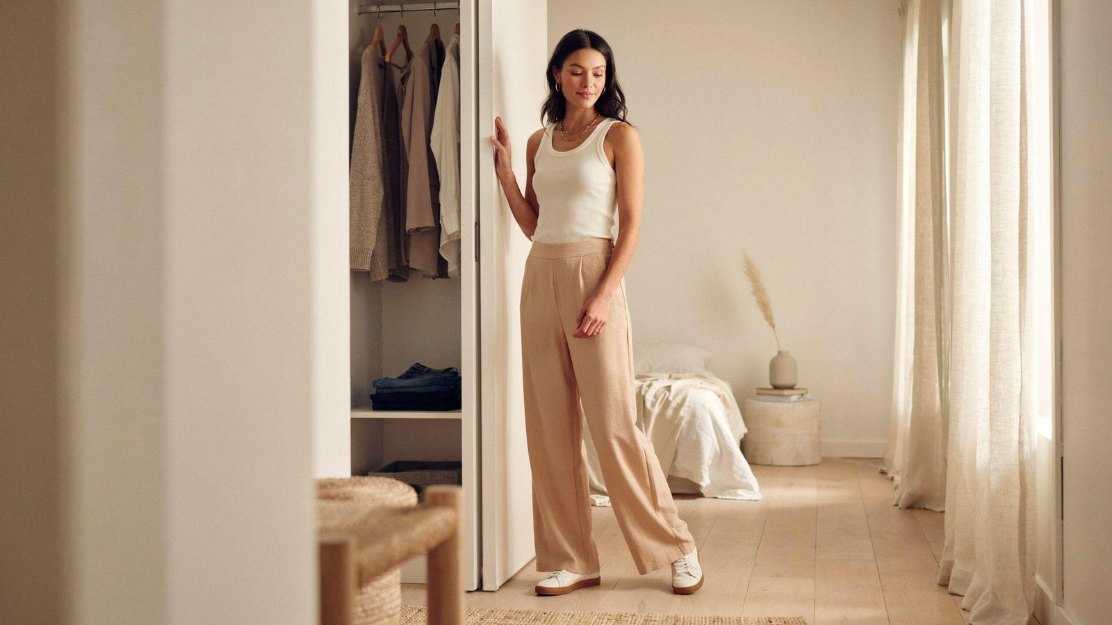 "Woman wearing casual wide leg pants with a fitted top and sneakers in a modern bedroom setting"