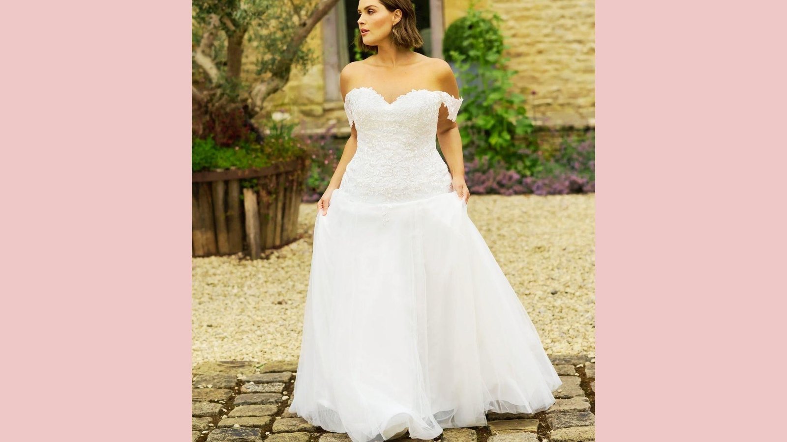 Plus-size bride in off-shoulder A-line gown with lace bodice, sweetheart neckline, tulle skirt, standing outdoors on gravel