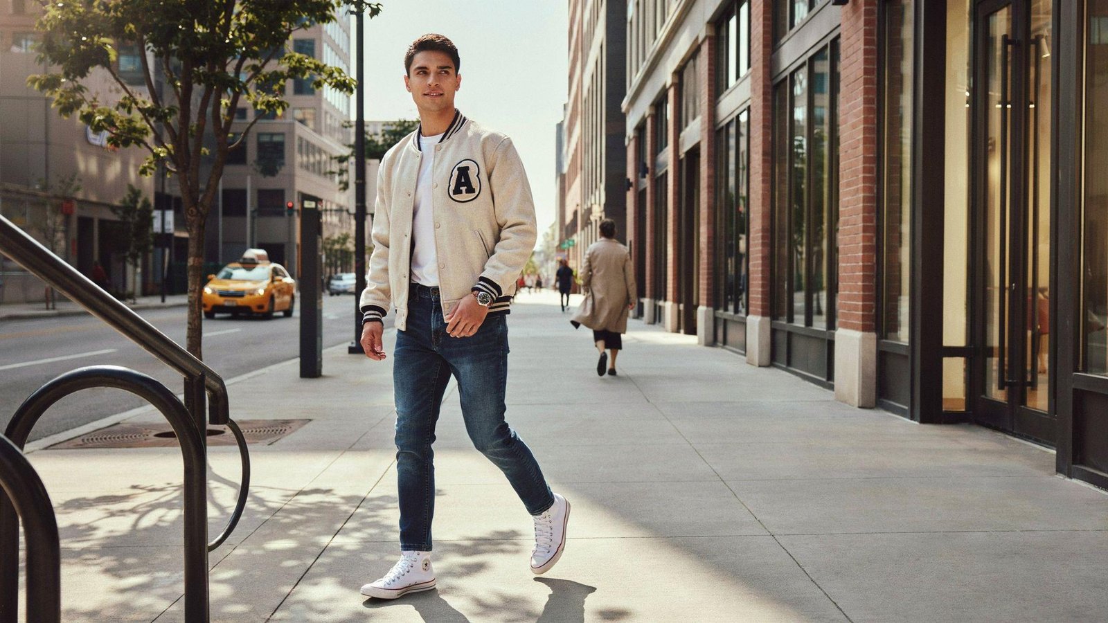 "Man wearing varsity jacket with high-top sneakers and jeans in a modern 80s-inspired streetwear outfit"