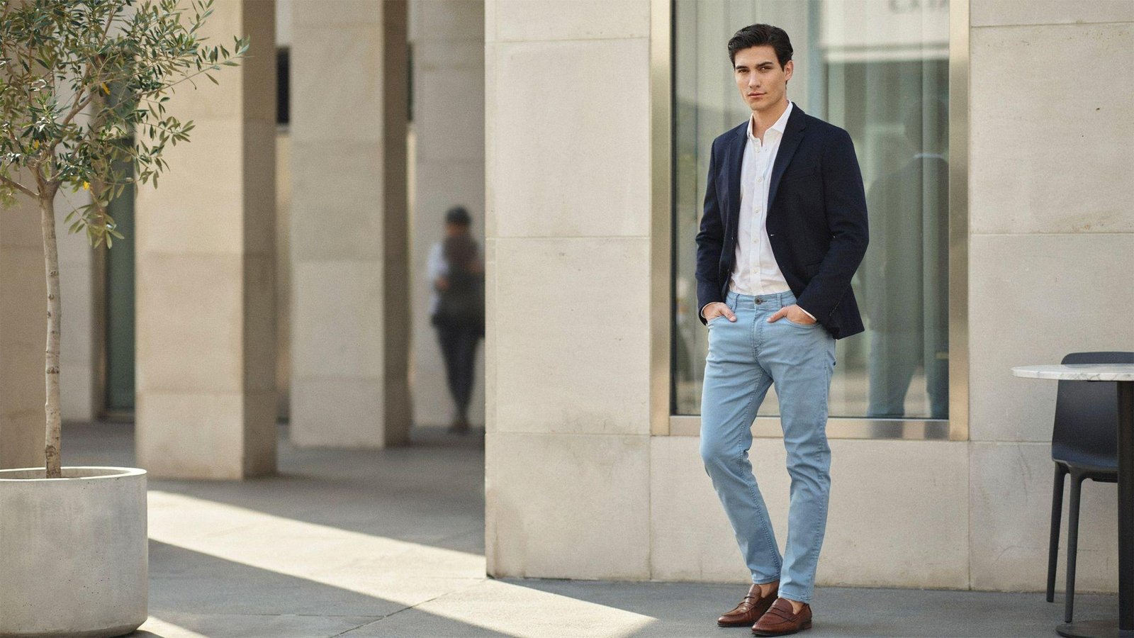 "Young man wearing light blue jeans styled with a navy blazer and white shirt in a smart casual urban outfit."