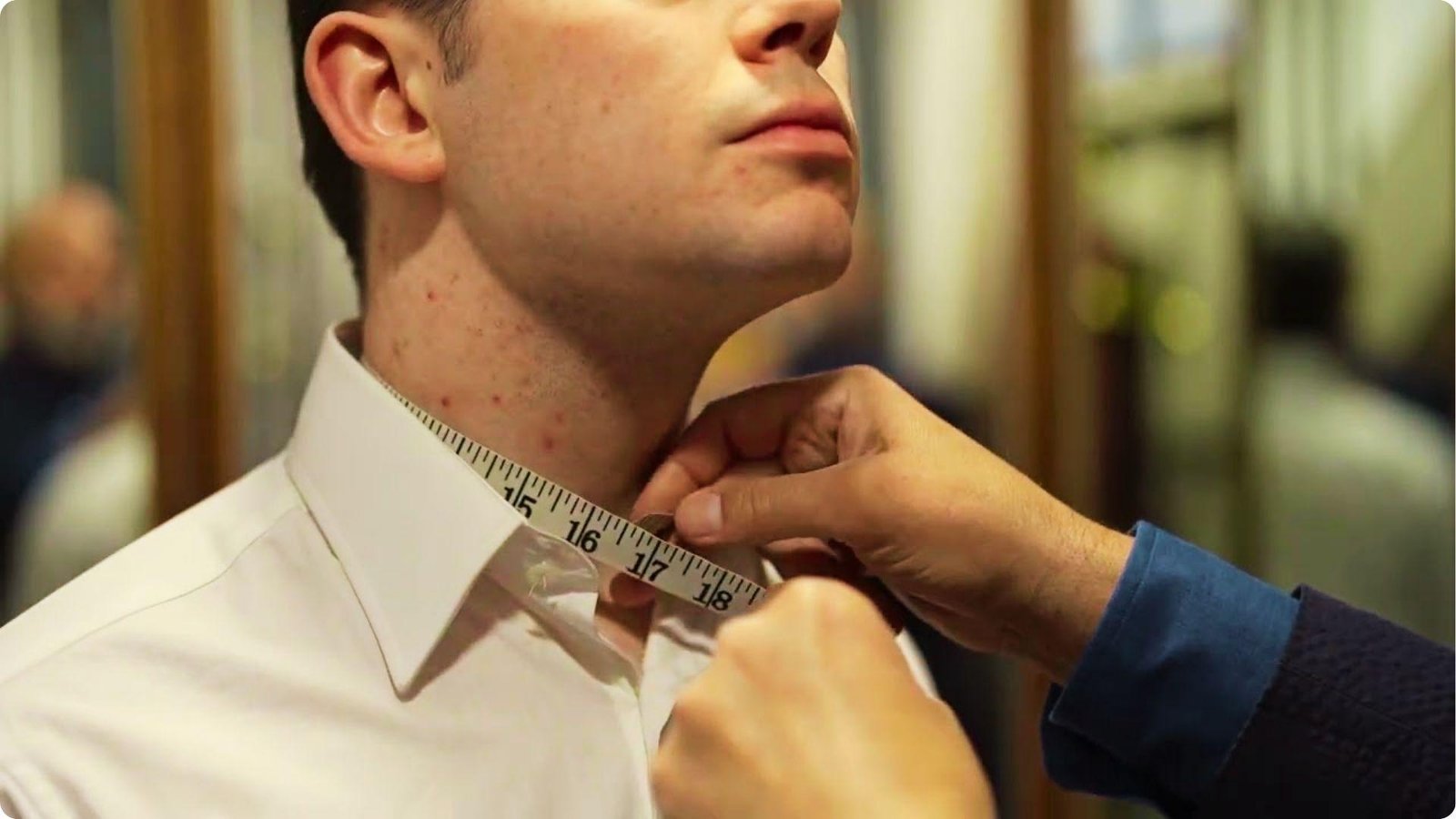 Tailor measuring a man’s neck with a measuring tape around the collar of a dress shirt.