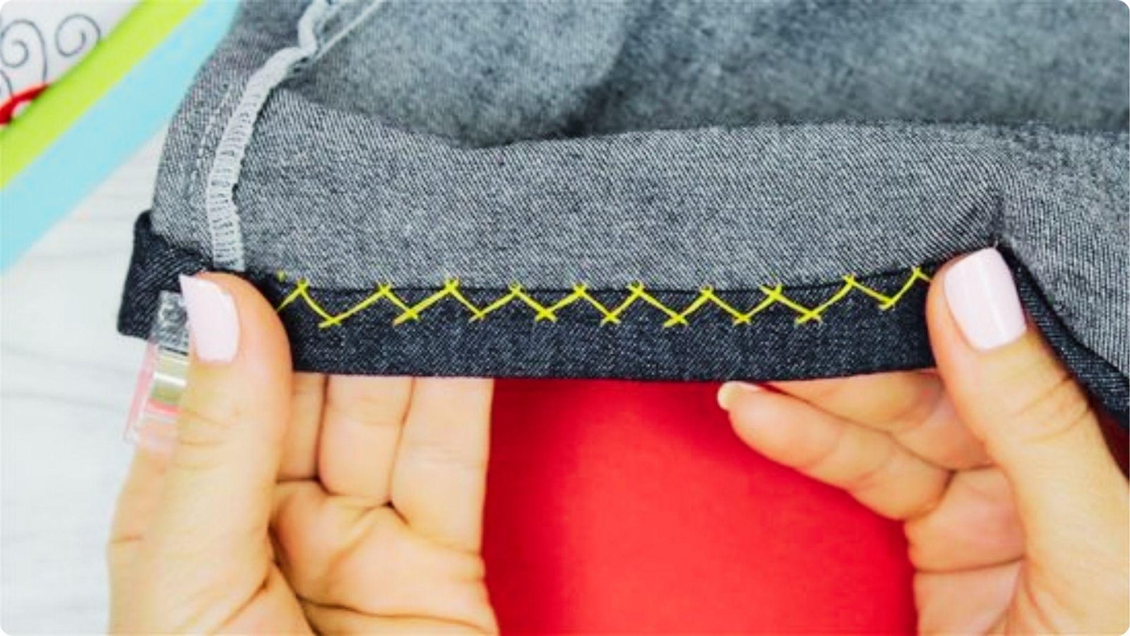 Close-up of hands holding a folded pant leg with bright yellow cross-stitch hemming.