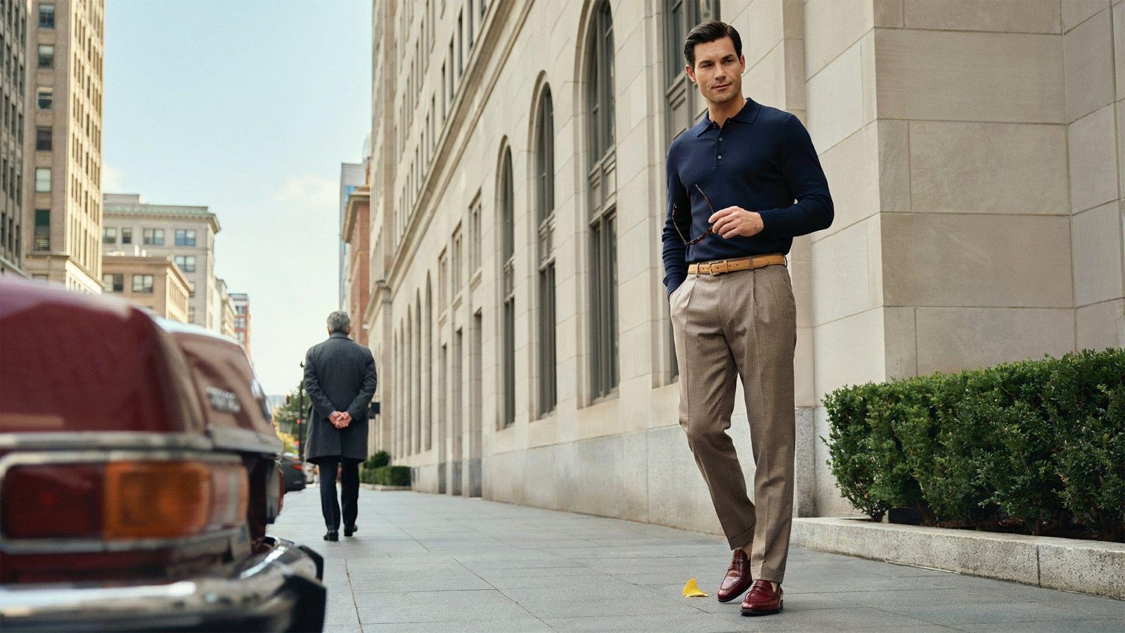 "Man wearing tucked-in polo shirt with pleated trousers and loafers in a clean 80s-inspired smart casual outfit"