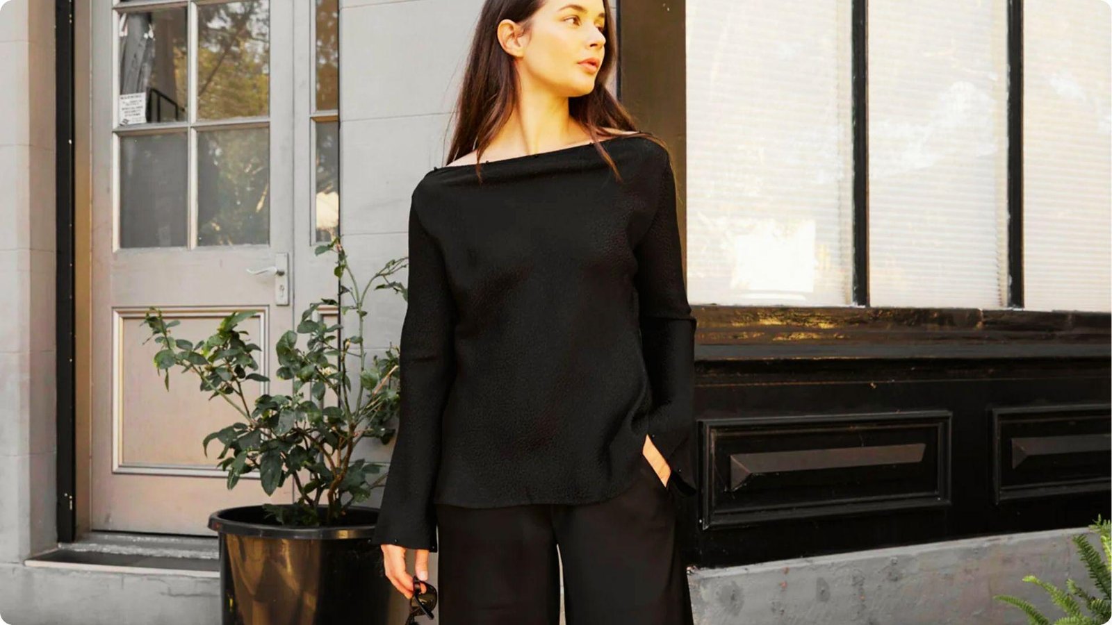 Woman in a black off-shoulder top and wide-leg pants standing outside a building.