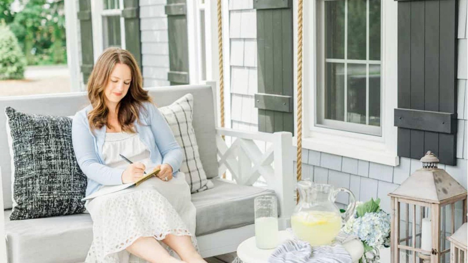A woman sitting and writing on her patio in a comfortable coastal grandmother styled outfit.