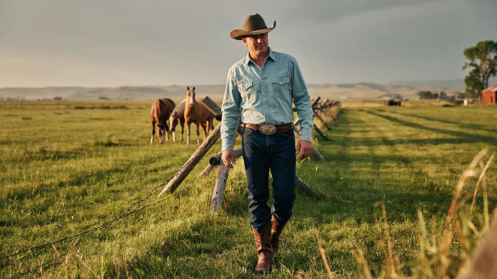 Cowboy wearing a classic Western outfit with boots, jeans, hat, and shirt on a ranch at sunset.
