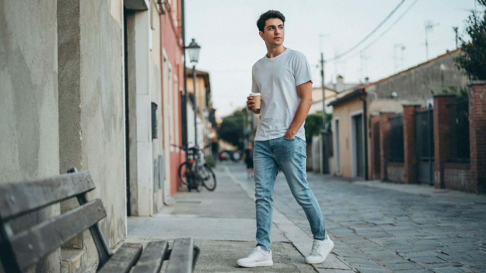 "Street style of a young man wearing light blue jeans with a white t-shirt and white sneakers in a casual urban setting."