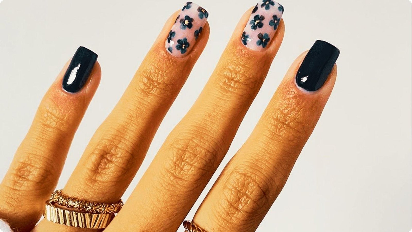 Close-up of a hand with glossy navy blue nails and delicate floral nail art on a nude base.