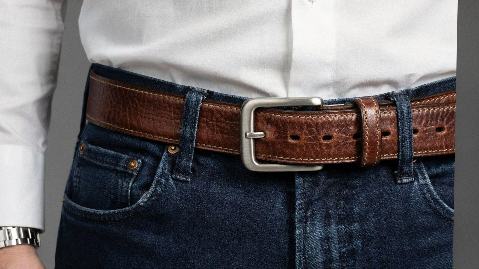 "Close-up of a stylish polished belt buckle paired with dark jeans and a tucked-in shirt"