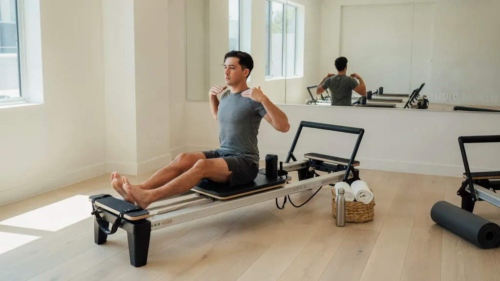 Man performing reformer Pilates in fitted tee and compression shorts.