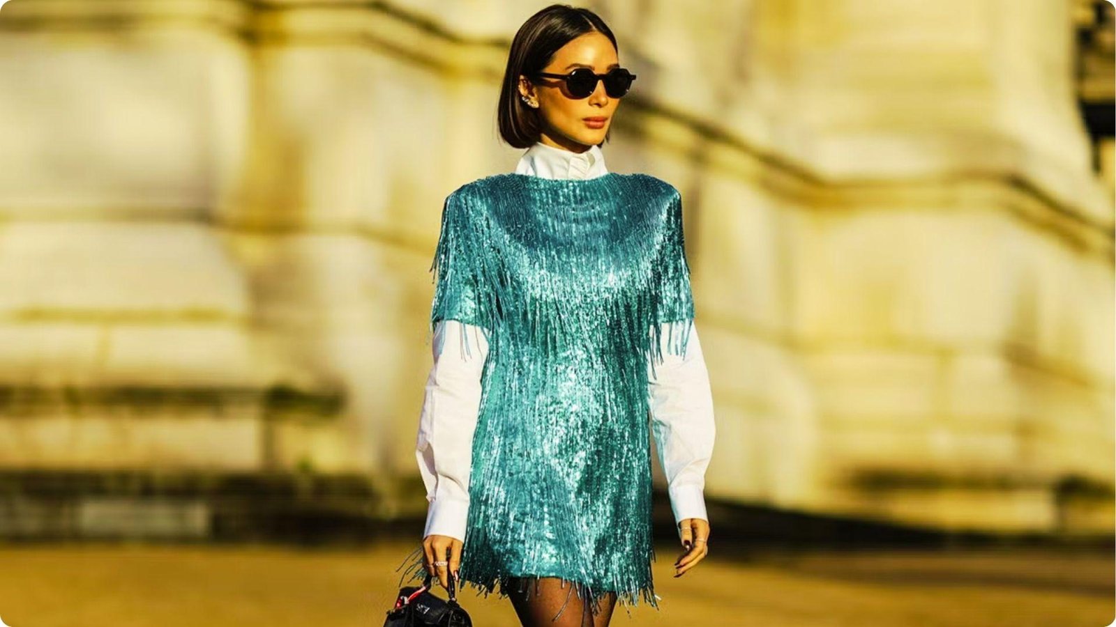 Woman standing outdoors in a teal sequin fringe mini dress layered over a crisp white collared shirt.