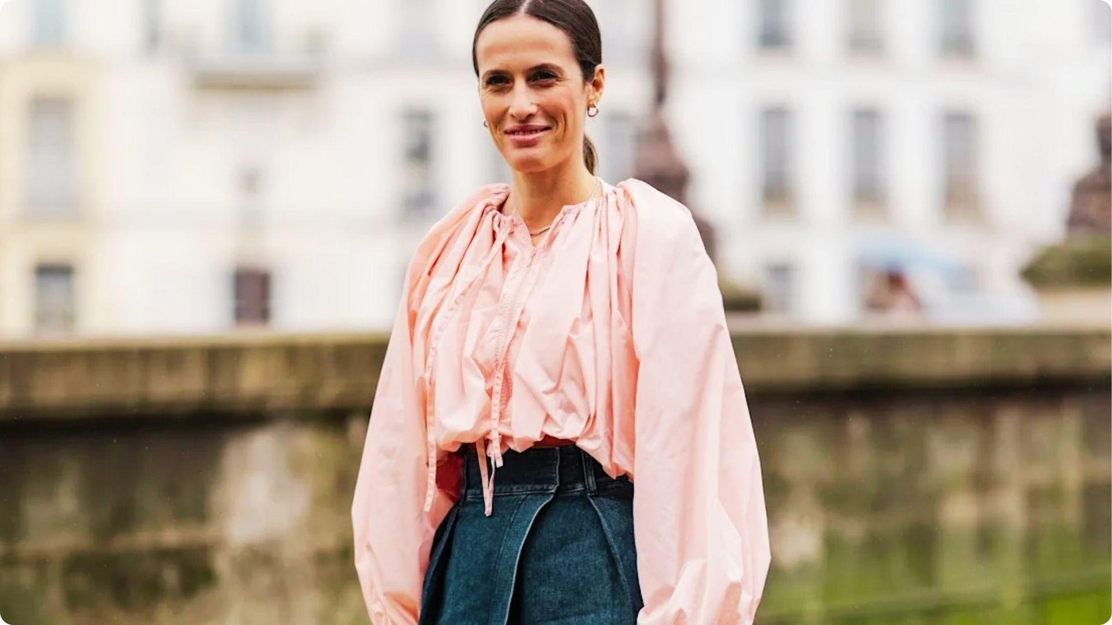 Woman stands outdoors in a breezy light pink blouse tucked into dark denim blue pants.