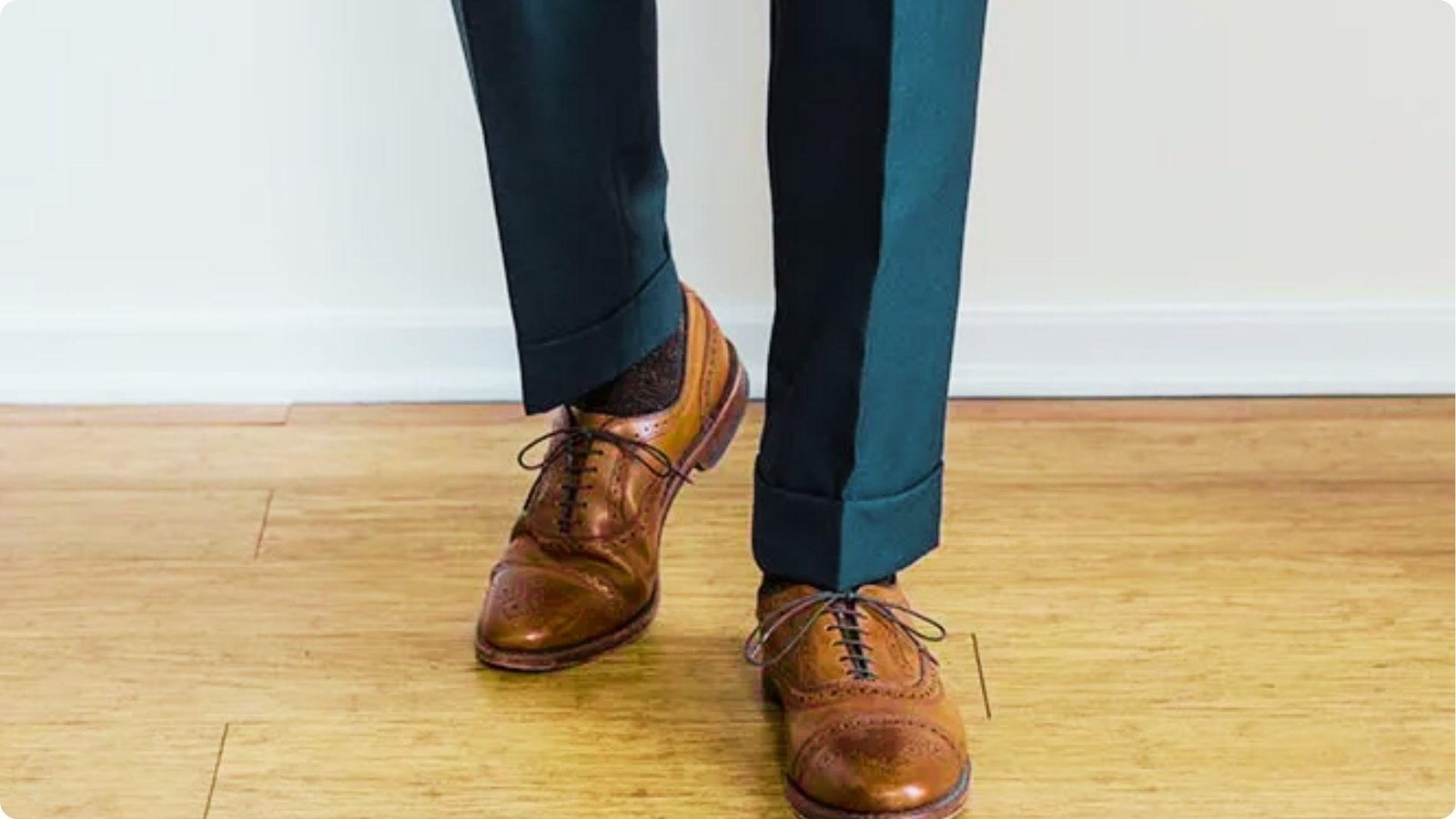 Close-up of teal dress pants with a clean 1.5-inch cuff resting on brown leather oxford shoes.