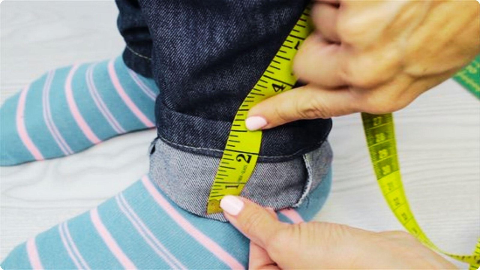 A yellow measuring tape checks the length of a cuffed pant leg worn over striped socks.