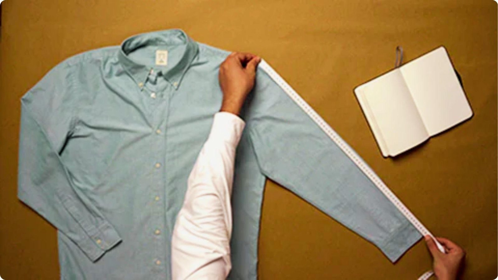Overhead view of a blue dress shirt laid flat with measuring tape along the sleeve.