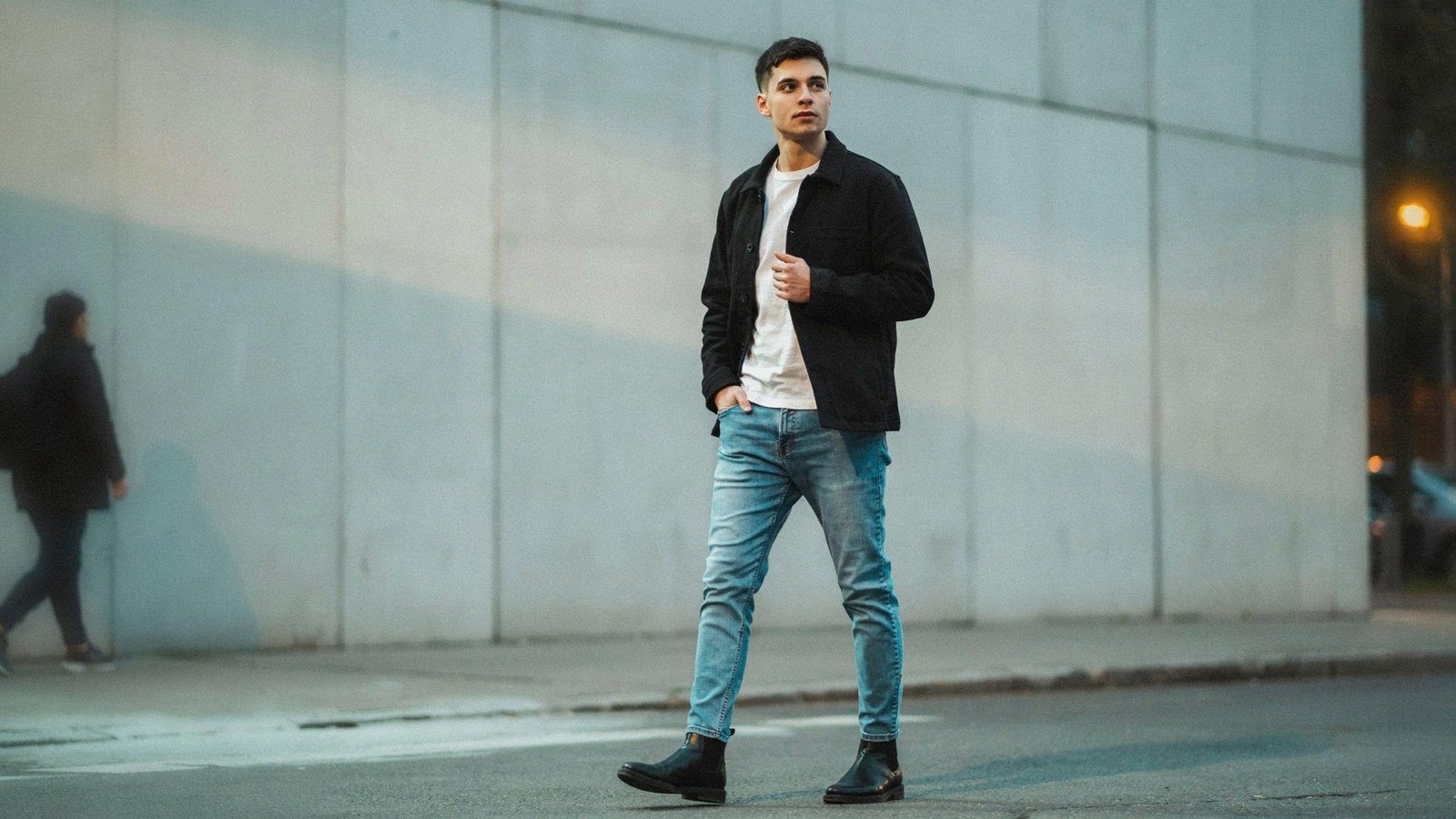 "Young man wearing light blue jeans with a white t-shirt and black overshirt jacket styled for an evening urban look."