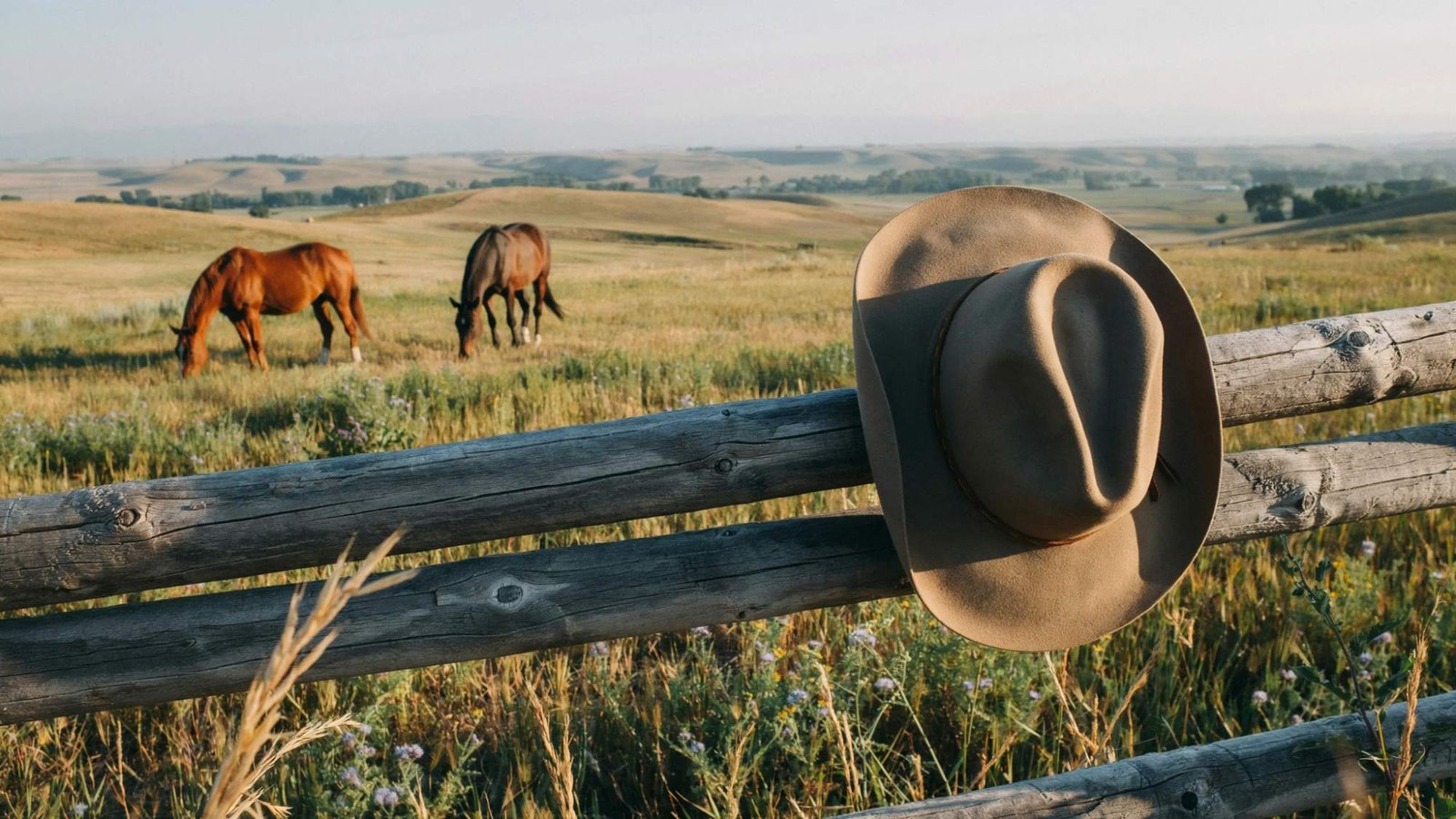 Classic cowboy hat displayed on a ranch fence at sunset.